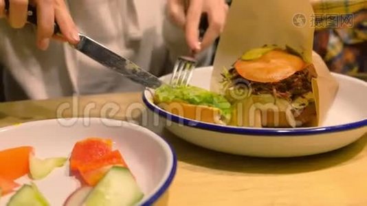 女人正在吃大汉堡，用叉子和刀在盘子上端着，双手特写。视频