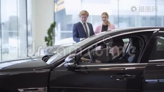 一对年轻成功的夫妇看着一个自信的女孩坐在驾驶座上一辆新的、昂贵`车的机舱里。视频