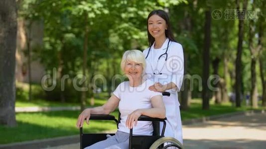 女护士和残疾老年妇女对着镜头微笑，在医院公园放松视频