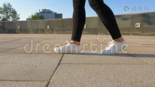 穿着白色鞋子`女人的腿正沿着一条干净、空荡荡的人行道走着。视频