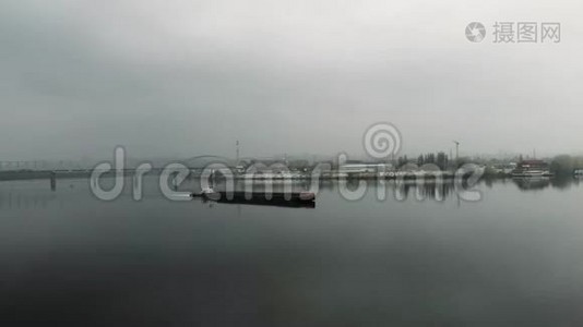 在市中心的工业烟雾中，铁驳船在空旷平静的河流上航行。 在市区的一座桥上飘浮着一片大雾视频