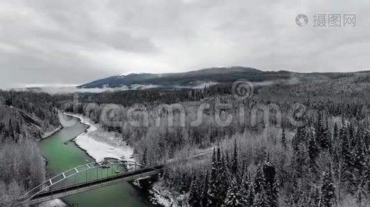 在白雪皑皑的山脚下茂密的松林中，Drone在一条翡翠河上卸下一座路桥视频