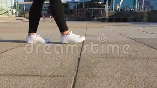穿着白色鞋子`女人的腿正沿着一条干净、空荡荡的人行道走着。视频