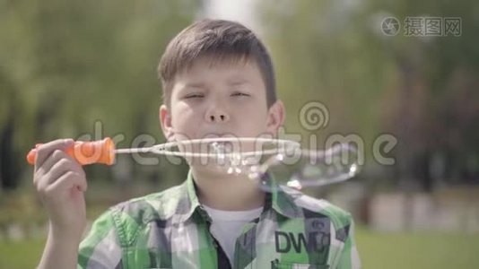 肖像可爱的小男孩穿着格子衬衫，把汤泡泡吹得很近。 这孩子在户外玩得很开心视频
