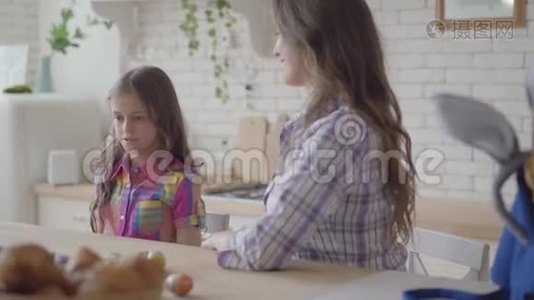 年轻的母亲和可爱的女孩坐在厨房里。 小女孩拿了两个复活节彩蛋给妈妈。 准备工作视频