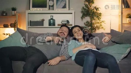 快乐的一对夫妇在晚上看电视，笑着在家玩着聊天视频