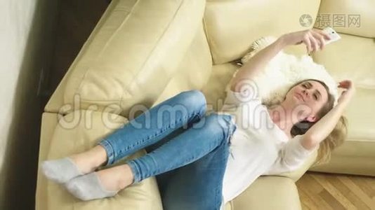 可爱的金发女孩躺在沙发上用手机自拍视频
