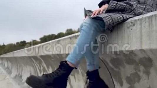 年轻女子坐在风中的水泥栅栏上，摇着腿视频