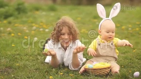 一岁的孩子穿着兔子服装，哥哥坐在公园里玩复活节彩蛋视频