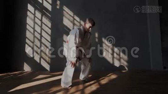 男勇敢运动员正在准备跆拳道比赛。 穿着白色和服，光着脚，阳光从窗户射进来视频