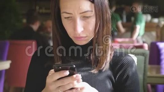 年轻的馄饨在工作休息的时候坐在舒适的咖啡店里，一边用手机，一边迷人的快乐女性阅读视频