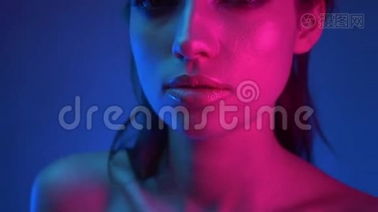 特写镜头在模特的侧面蓝色和粉红色霓虹灯注视着镜头伸出它。视频