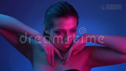 模特用蓝色和粉红色的霓虹灯，她的手广泛的姿势时尚地进入相机。视频