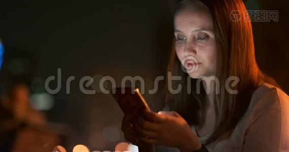 年轻女子晚上坐在城里，拿着智能手机视频