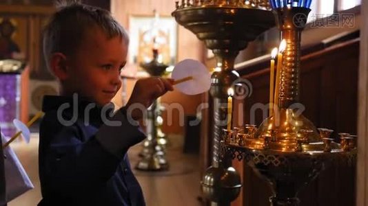 小男孩拿着蜡烛在东正教教堂的图标前祈祷，燃烧并点燃蜡烛。 中弹。视频
