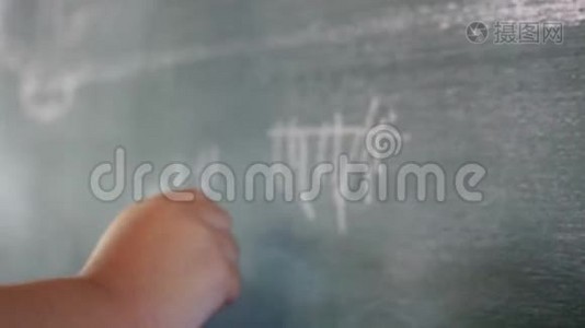 一个可爱的小女孩在学校用白色粉笔在黑板上画画。视频