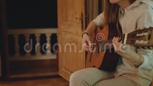 戴眼镜的金发女孩在舒适的公寓里弹吉他，在椅子上唱歌。 一个女人在室内创作音乐视频