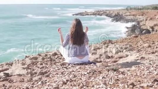 一个年轻的女人正坐在海边悬崖上的莲花座上。视频