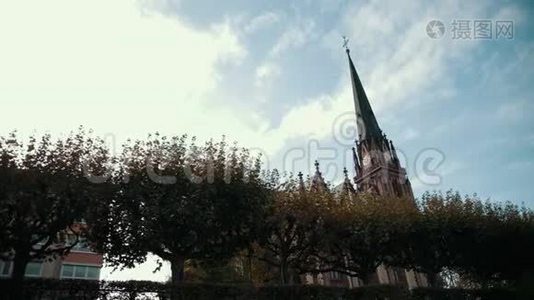 哥特式风格的旧教堂。 有尖顶和时钟。 前景是树木视频