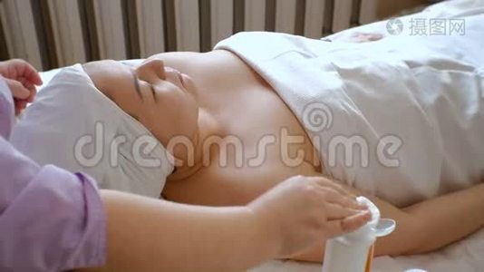 美容师的手湿润了棉垫。 一个美容院里的亚洲女孩躺在沙发上。 清洗和r的过程视频