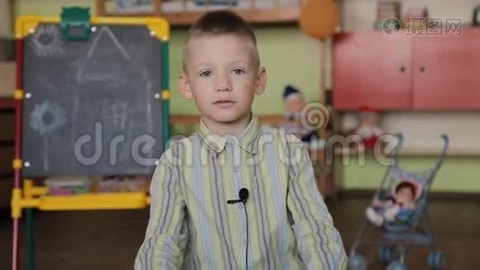 一个穿格子衬衫的男孩坐在相机前的椅子上，衣服上有麦克风，回答问题。视频