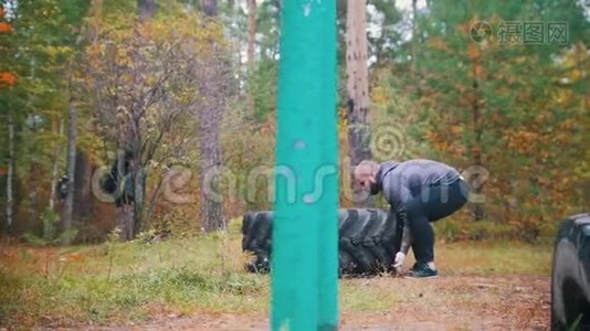 一个纹身男健美运动员推着卡车轮胎在地上-训练在秋天的森林视频