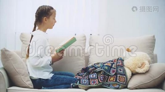 可爱的小女孩坐着，双腿蜷曲，为她的泰迪读童话故事，有感情地移动她的手，表现出视频