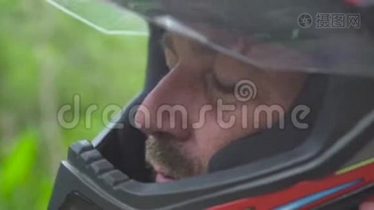 近距离面对骑摩托车的男子，戴着摩托头盔，看着相机和微笑。 戴着防护帽的莫托摩托车手视频