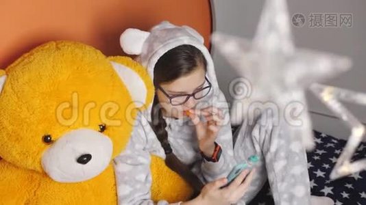 在一个寒冷的冬夜，穿着温暖的睡衣的女孩，坐在一只大泰迪熊的怀里，吃着橘子和睡衣视频