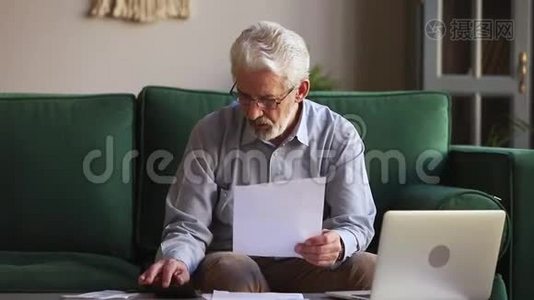 一位严肃的老人手里拿着纸，在家里计算家庭账单视频