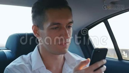 年轻的商人在开车时使用他的智能手机。 男人正在检查指甲、帽子或新衣服视频