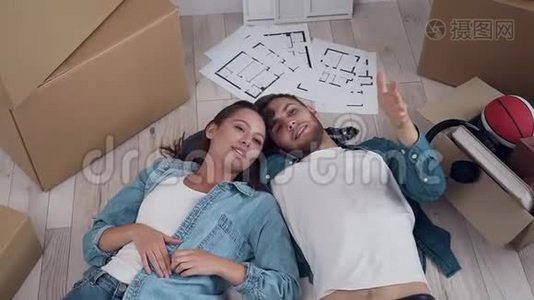 幸福夫妇躺在新公寓的地板上，在移动过程中交谈和环顾四周。 关系和住房视频