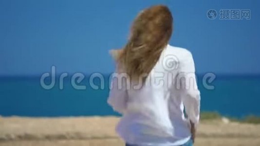 一个年轻的女孩跑到美丽的大海上面的悬崖。 在风中美丽地发展头发。视频