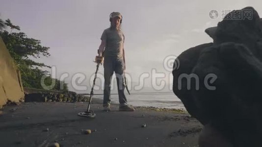 带金属探测器的人在日出时带着他的狗在废墟中寻找海洋热带沙滩上的宝藏。视频