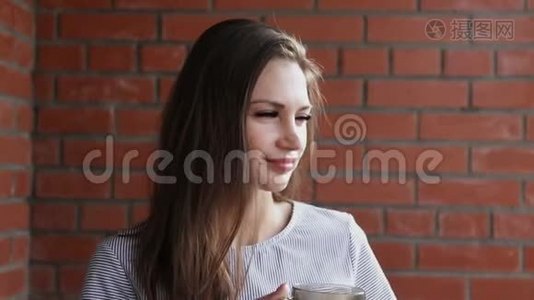 美女端着一杯热茶.. 一个女孩在砖墙上喝茶视频