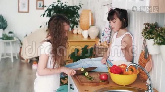 小女孩在厨房的木板上割黄瓜，姐姐坐在桌子上，慢动作视频