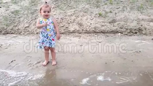 一个小女孩穿着一件花裙子站在河岸上的洞穴里，很高兴。视频