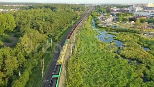 在阳光明媚的夏天，一列有建筑材料的火车在田野和森林的背景下乘火车行驶视频