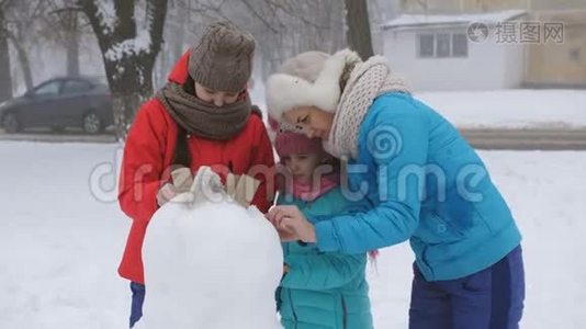 妈妈和两个女儿在冬天装饰鹅卵石一起堆雪人。视频