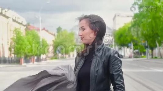在一个阳光明媚的夏天，穿着黑色皮夹克的苗条迷人女孩沿着城市的街道散步。视频