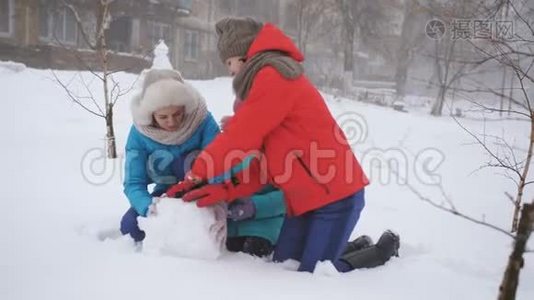 父母和孩子在雪地里玩耍。 妈妈和两个女儿在冬天堆雪人。视频