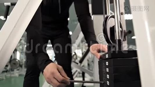男子`手在模拟器上减轻重量，引脚选择换板重量堆叠。 体育运动。视频