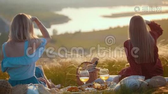 两个美丽的女人坐在田野上野餐-在日落时欣赏河景视频