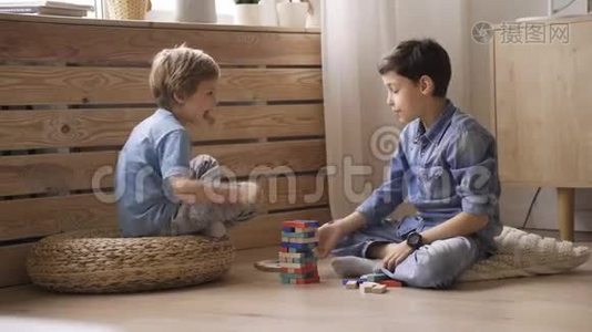 两个男孩的兄弟正在用坐在地板上的木块建造一座塔视频
