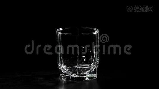 豪华威士忌。 手把金色的威士忌从一个方形的瓶子里倒入旋转的黑色桌子上的玻璃杯里。 不倒翁威士忌。视频