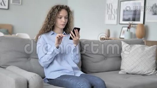 年轻的卷发女士在沙发上放松时打电话视频