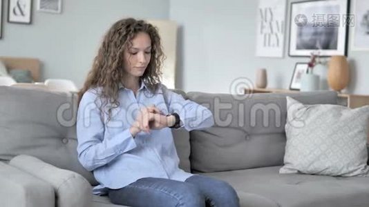 卷发女人坐在沙发上用智能手表视频