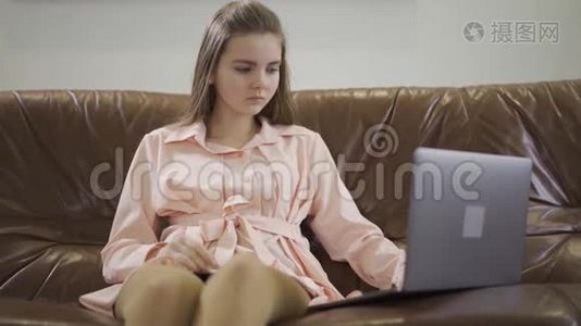 漂亮的女孩坐在笔记本电脑前的皮革沙发上。 现代少年的休闲.. 对小玩意的上瘾视频