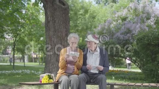 肖像可爱的成年夫妇看着老照片，回忆着坐在公园长凳上的快乐时刻。 成熟的夫妻视频