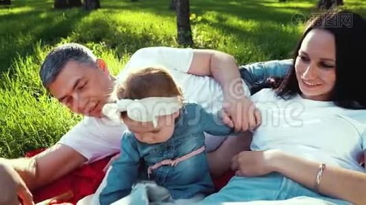 微笑的父母带着小女孩在公园草地上的毯子上放松视频